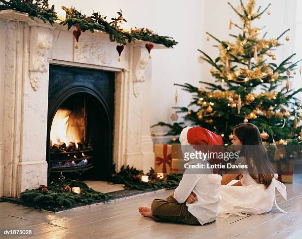 brother and sister sitting in front of a fireplace at christmas - pantalón decorado fotografías e imágenes de stock