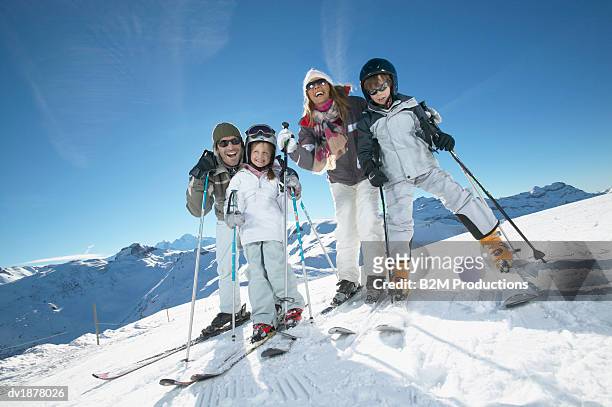 portrait of a family with two young children in skiwear standing on a ski slope - family winter sport stock pictures, royalty-free photos & images