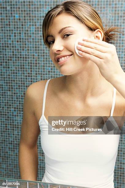 reflection of a young woman looking in a bathroom mirror and cleansing her face - cotton pad stock pictures, royalty-free photos & images