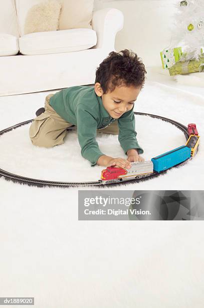 young boy in a white living room playing with a toy train set at christmas - christmas train set photos et images de collection