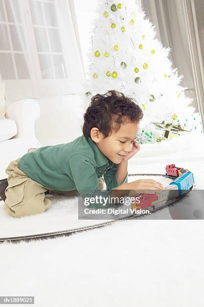 young boy kneeling on the floor of a white living room playing with a toy train set, at christmas - christmas train set photos et images de collection