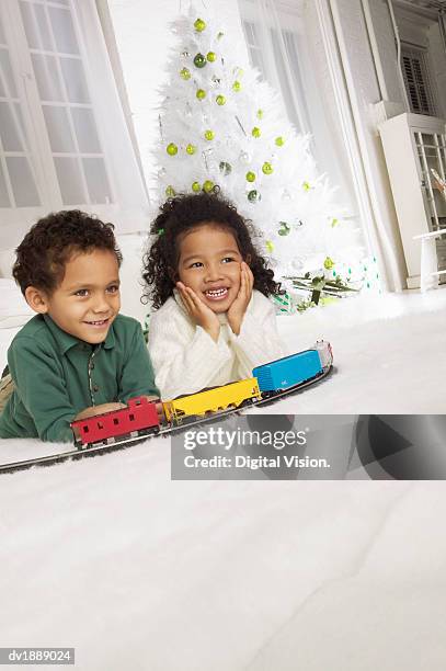 portrait of two young siblings playing with a toy train set on a living room floor at christmas - christmas train set photos et images de collection