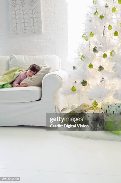 young girl sleeping on a sofa in a living room next to an artificial christmas tree - digital devices beside each other bildbanksfoton och bilder