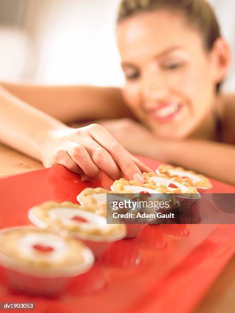 woman chooses a cherry bakewell tart from a row - adam berry stockfoto's en -beelden