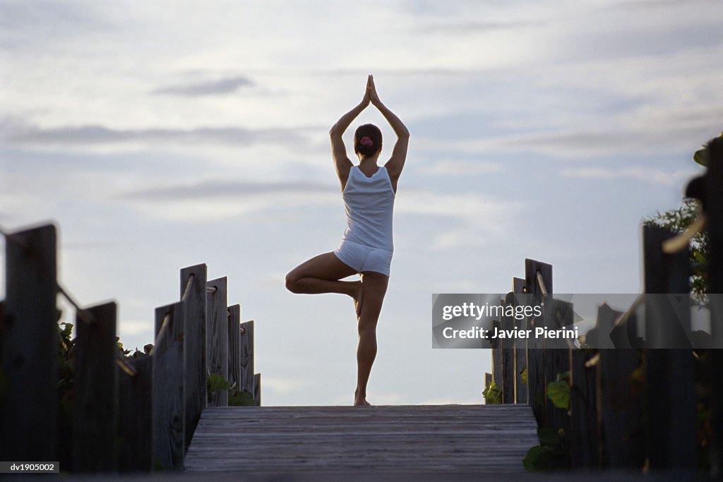 Rear View of a Young Woman Stands on a Boardwalk in a Yoga Pose