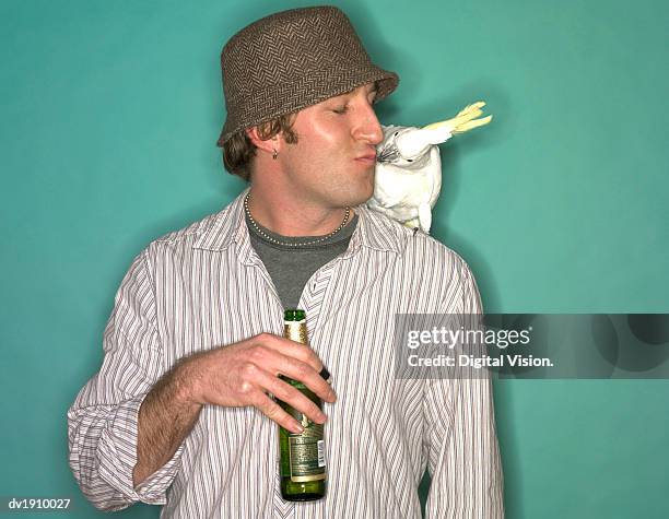 young man holding a beer bottle kissing a cockatoo - cockatoo stock-fotos und bilder