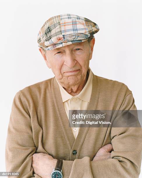 senior man wearing a flat cap standing with his arms crossed - platte pet stockfoto's en -beelden
