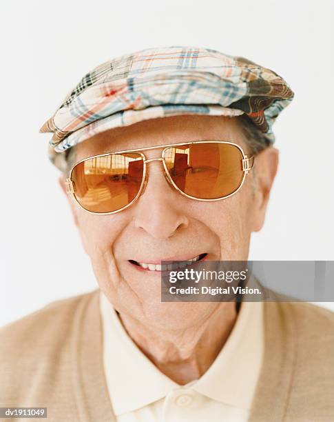 smiling senior man wearing sunglasses and a flat cap - flat cap stock-fotos und bilder