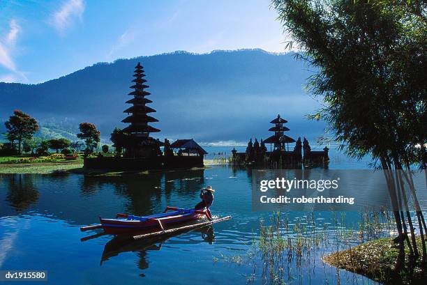 man in boat rowing and hindu temples at lake bratan, pura ulu danau, bali - bratansee stock-fotos und bilder