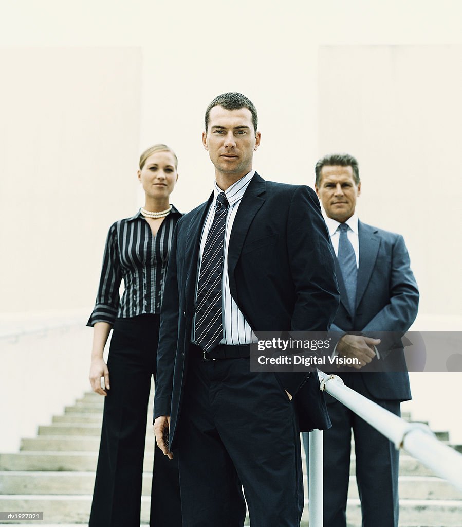 Businessman Standing on Steps in Front of Two Other Business Executives