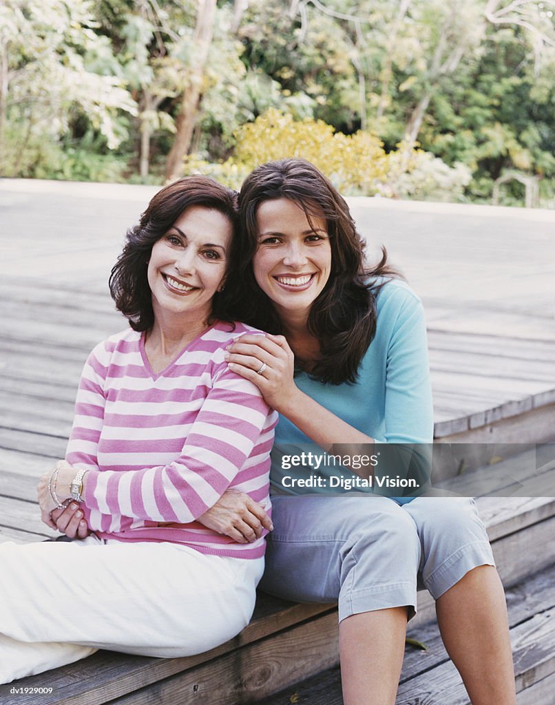 Mature Daughter Sitting on Wooden Decking in a Garden With Her Mother