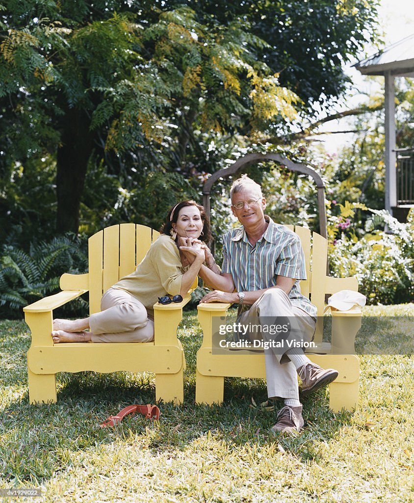 Senior Couple Sitting in Chairs Holding Hands on Their Garden Lawn