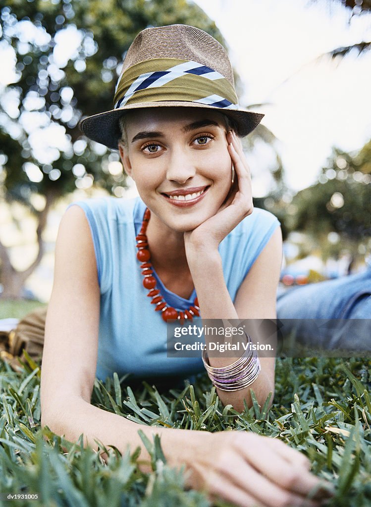 Young Woman Lying on Grass in a Park Wearing a Trilby Hat