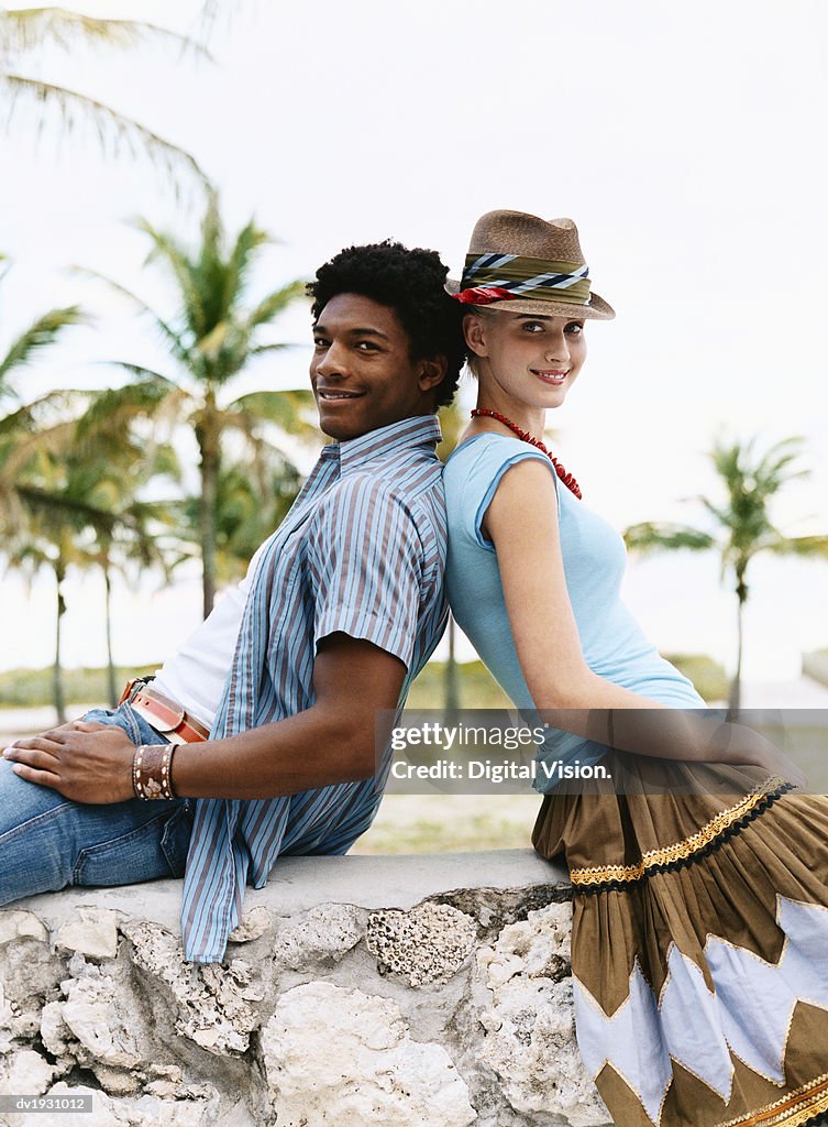 Young Man and Woman Sit Back to Back on a Stone Wall, Leaning on Each Other