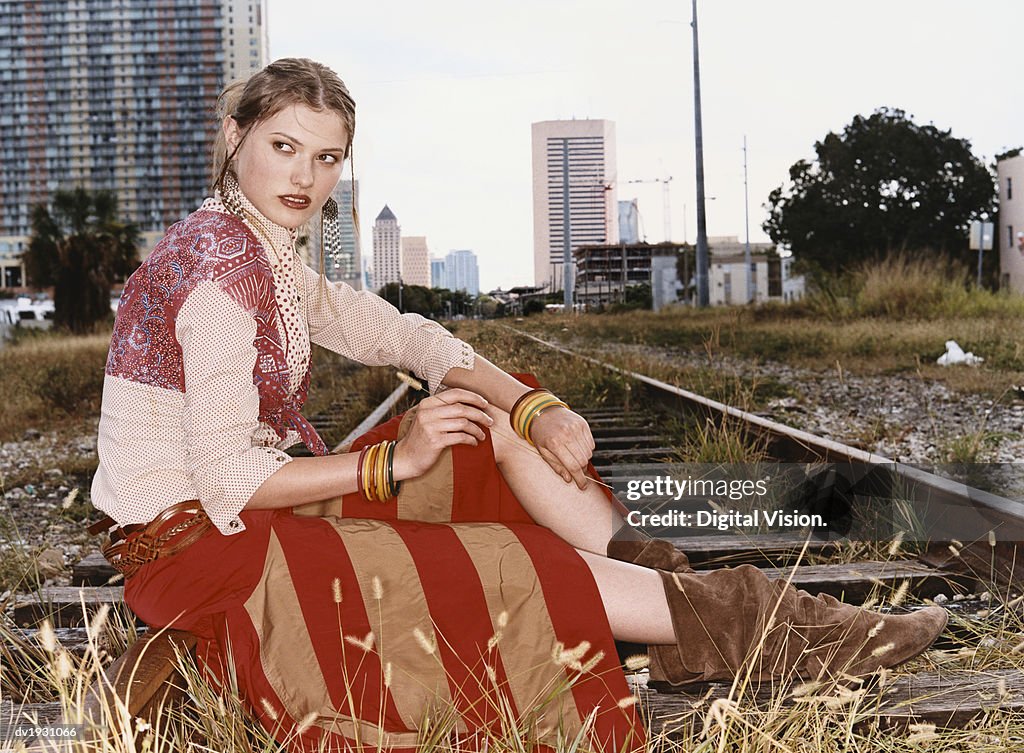 Side View of a Fashionable Woman Sitting on Urban Railway Tracks