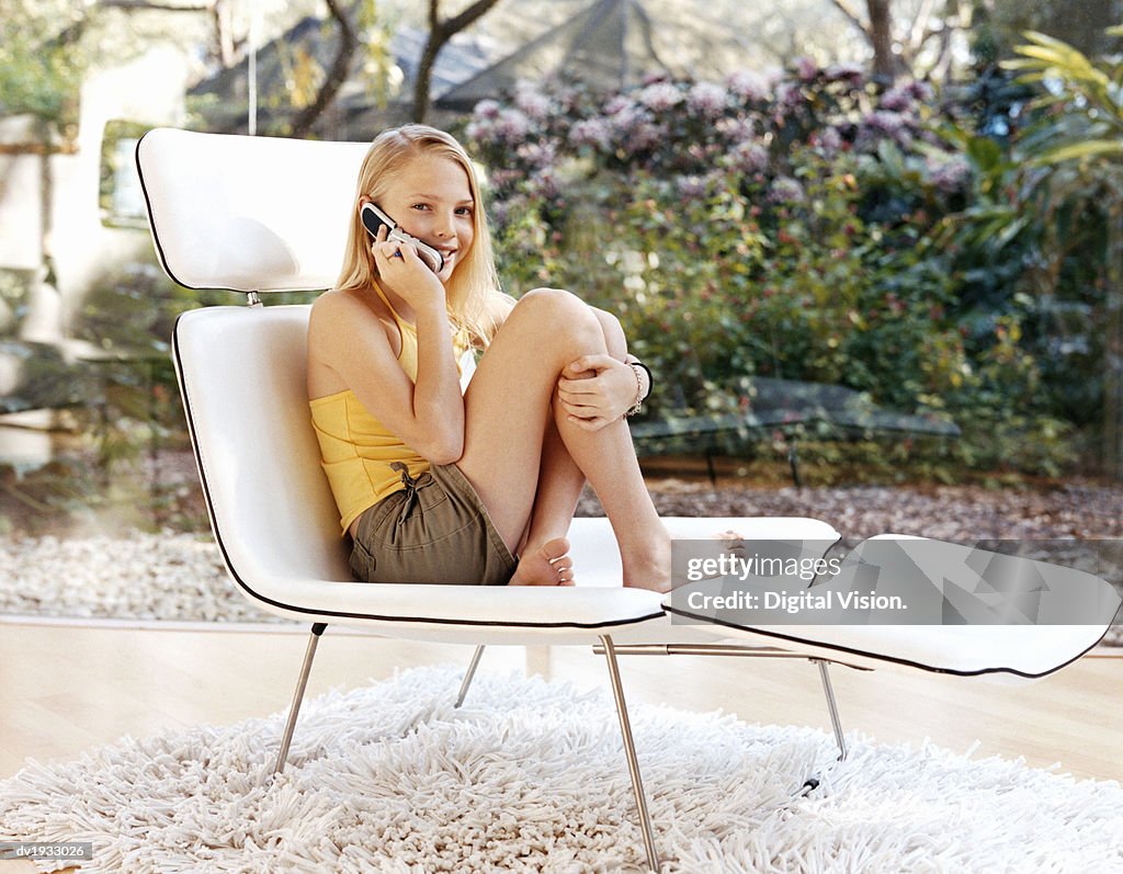 Young Teenage Girl Sitting on a Lounger Chair Using a Mobile Phone
