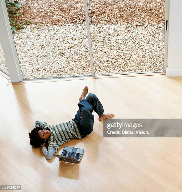 young boy lying on a wooden floor next to a laptop computer - digital devices beside each other bildbanksfoton och bilder