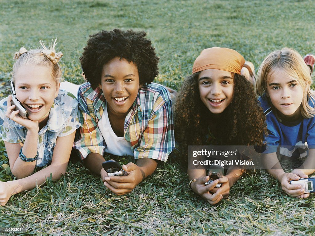 Four Young Boys and Girls Lie on the Grass in a Line, Holding Mobile Phones