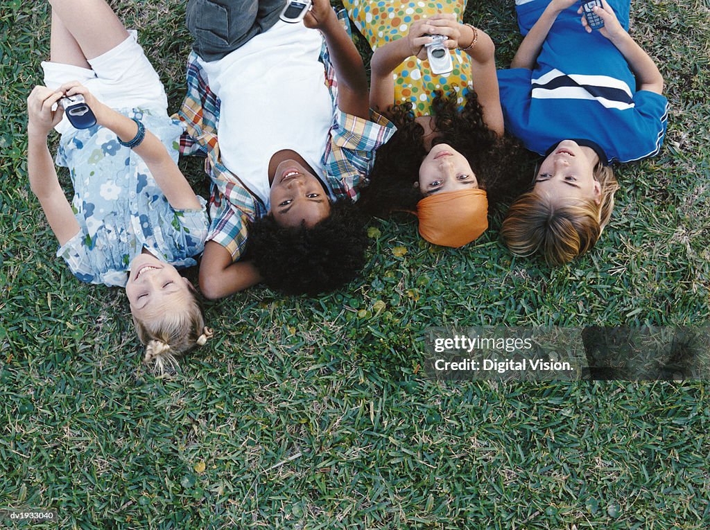 Overhead Shot of Four Young Friends Lying in a Row and Holding Mobile Phones