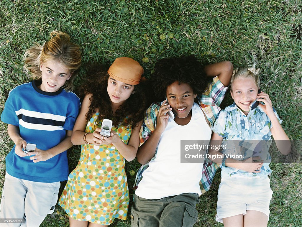 Four Young Friends Lying Together on Grass, Using Mobile Phones
