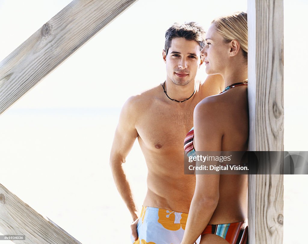 Portrait of a Young Man Standing by a Woman in a Bikini Below a Boardwalk