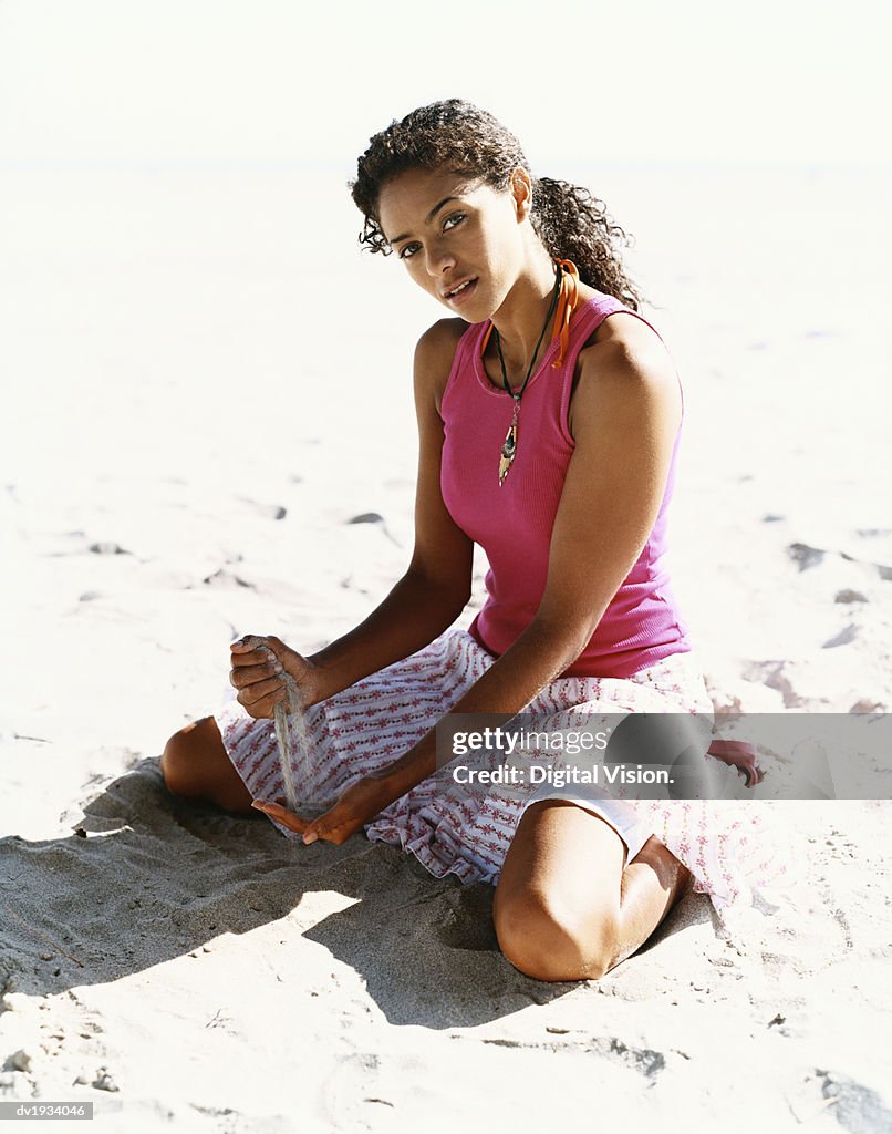 Young Woman Kneels on the Sand, Pouring it Through Her Fingers