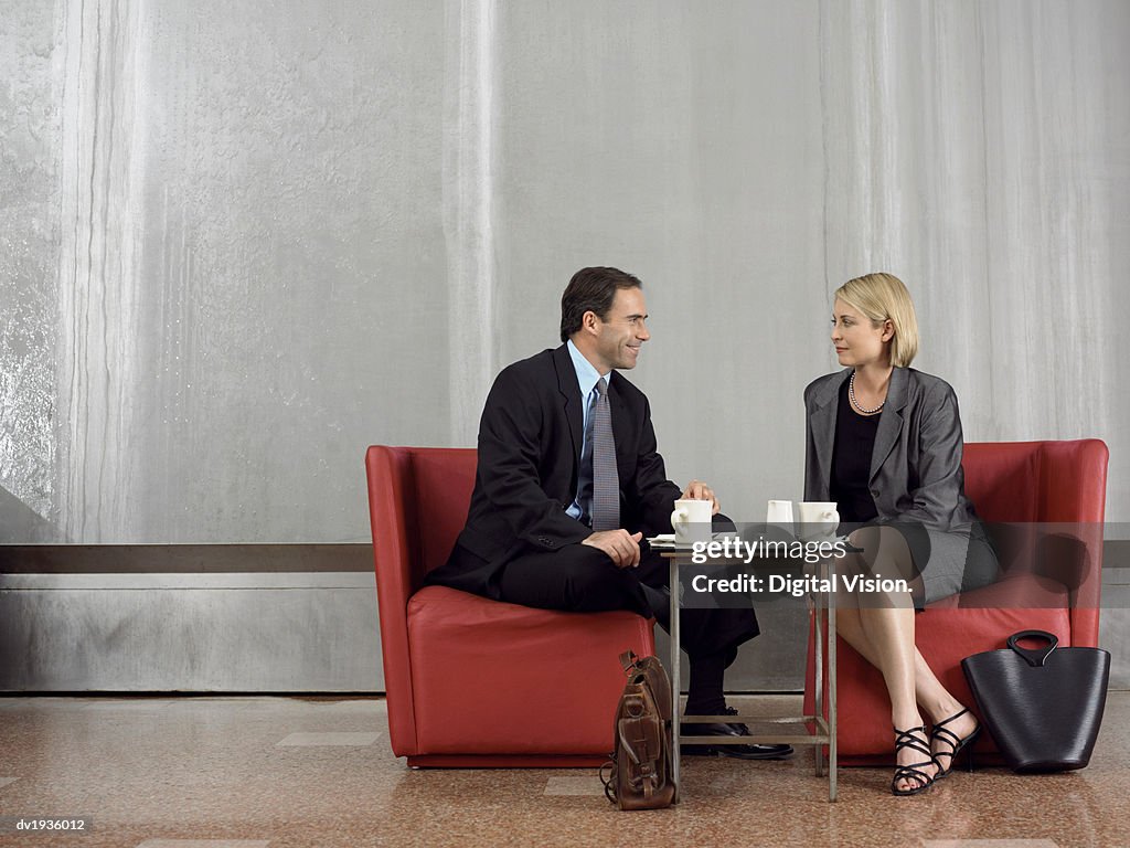 Two Business Colleagues Sit Face-To-Face on Chairs at a Coffee Table