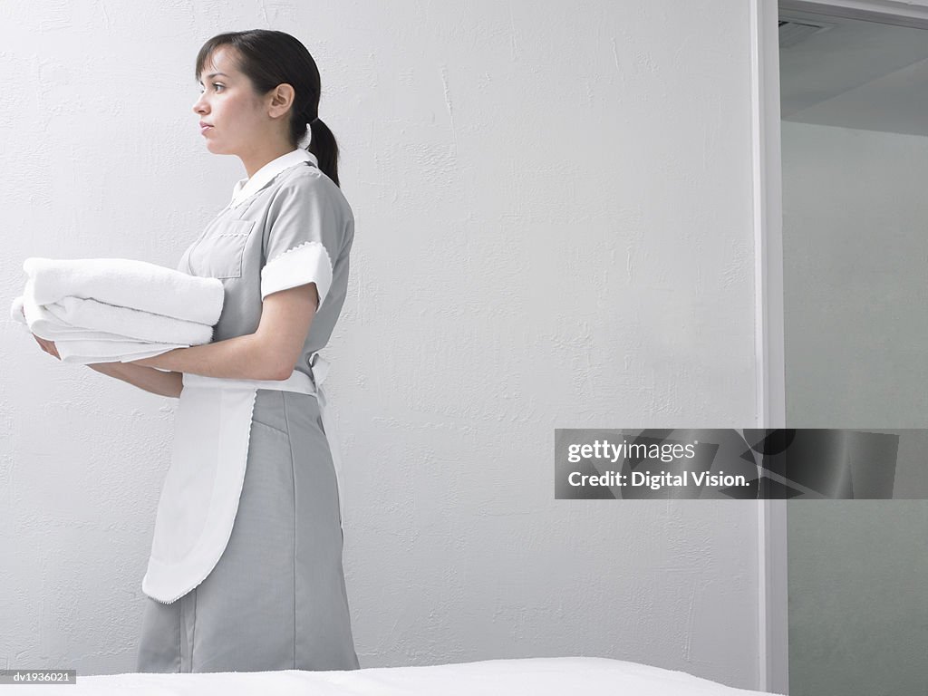 Side Profile of a Chambermaid in Uniform Walking With a Stack of Folded Towels