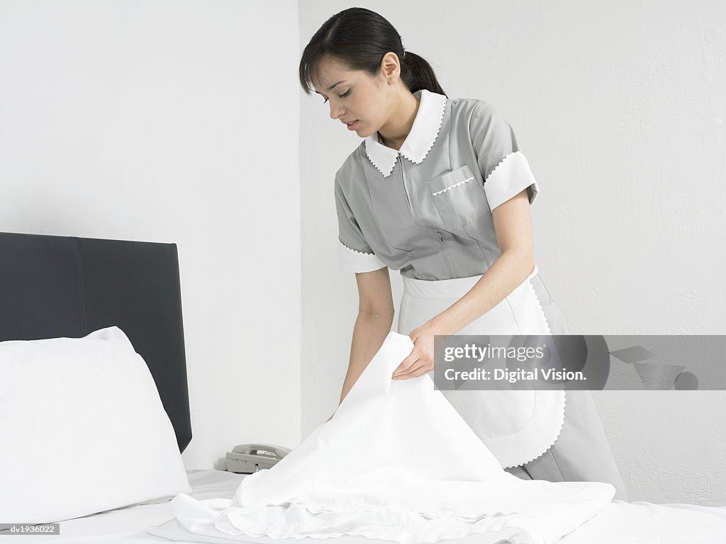 Maid Changing Sheets on a Bed in a Hotel Room