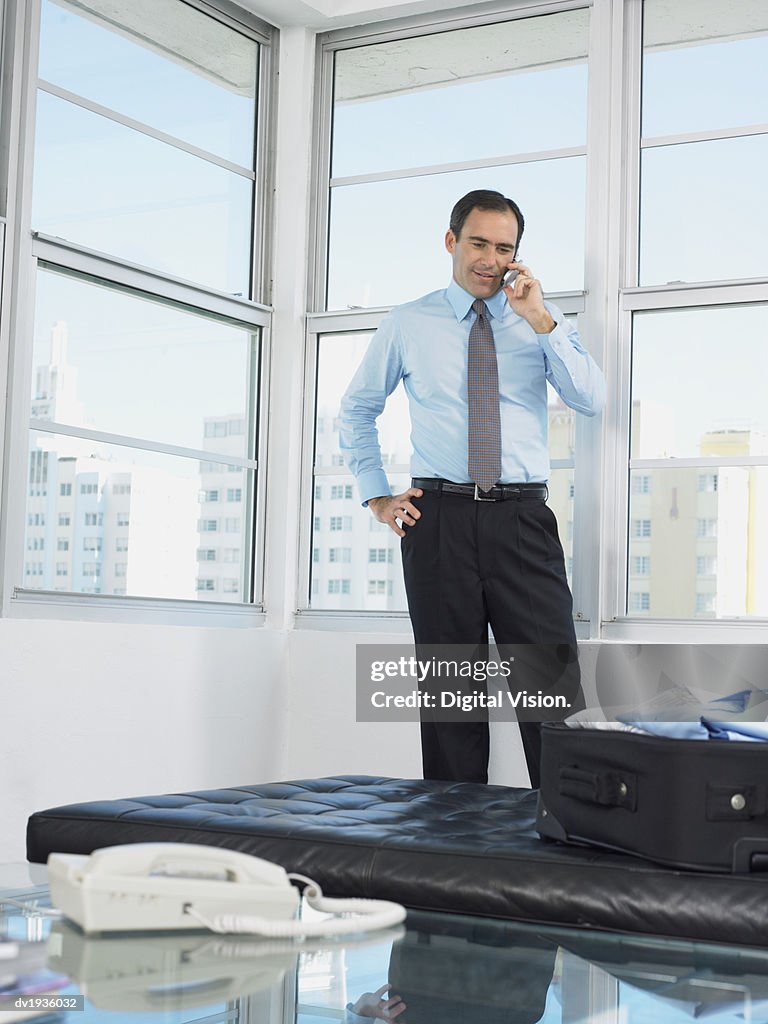 Businessman Stands by a Window in a Hotel Room Talking on His Mobile Phone