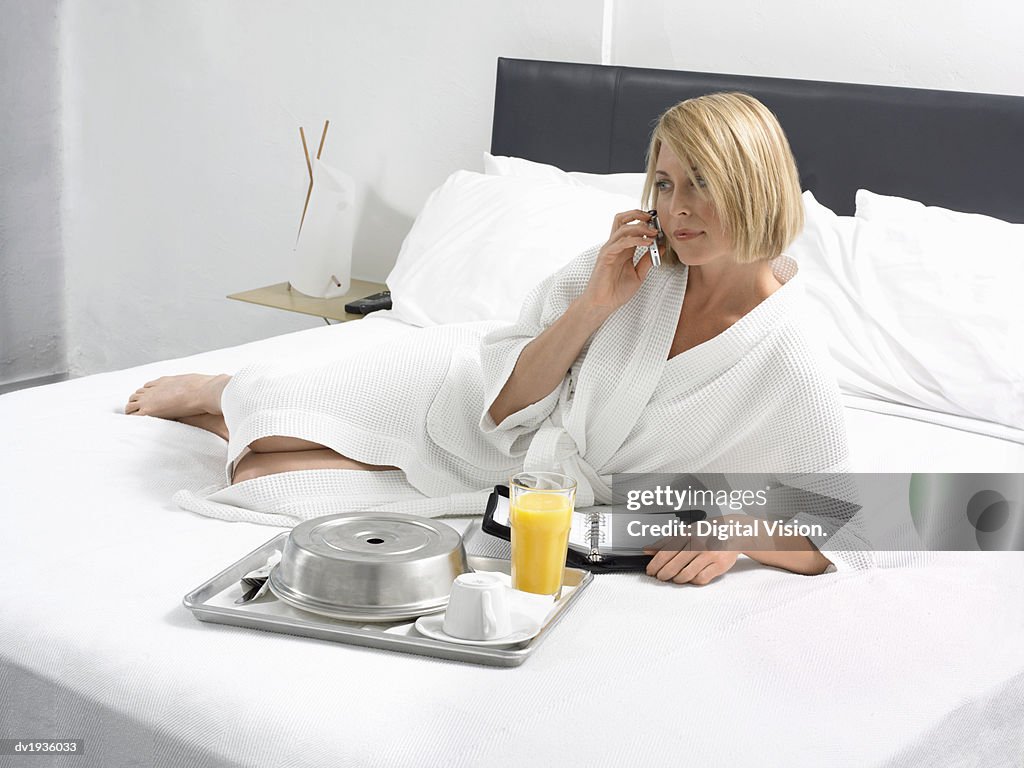 Businesswoman Lies on a Bed in a Hotel Room With a Breakfast Tray and Wearing a Dressing Gown