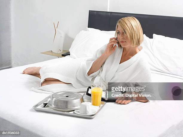 businesswoman lies on a bed in a hotel room with a breakfast tray and wearing a dressing gown - dressing up ストックフォトと画像