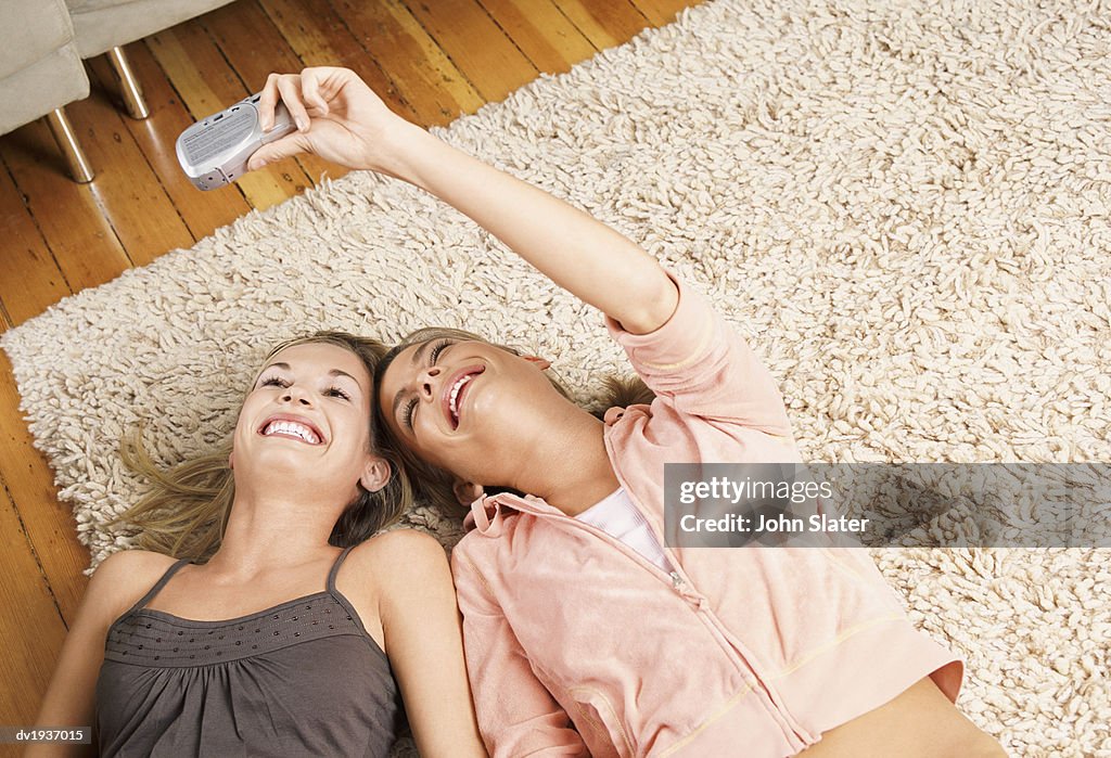 Twentysomething Female Friends Lying on a Rug Photographing Themselves