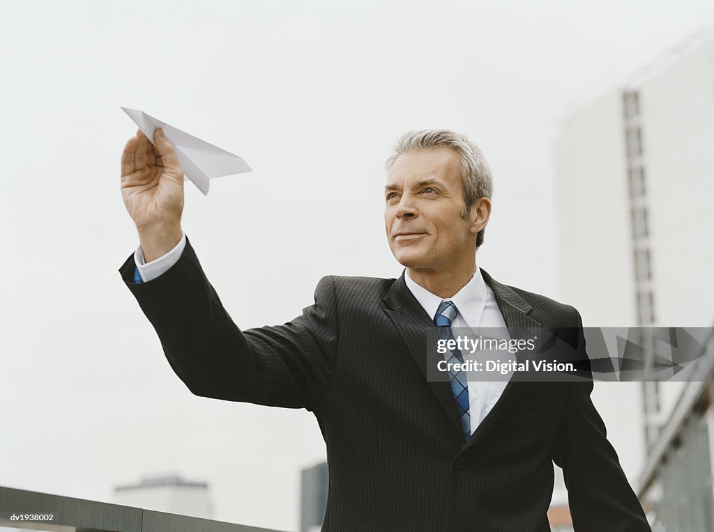 Mature Businessman Stands Outdoors Aiming a Paper Airplane