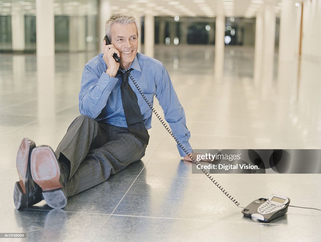 Businessman Holding a Phone Receiver Sitting in an Empty Office