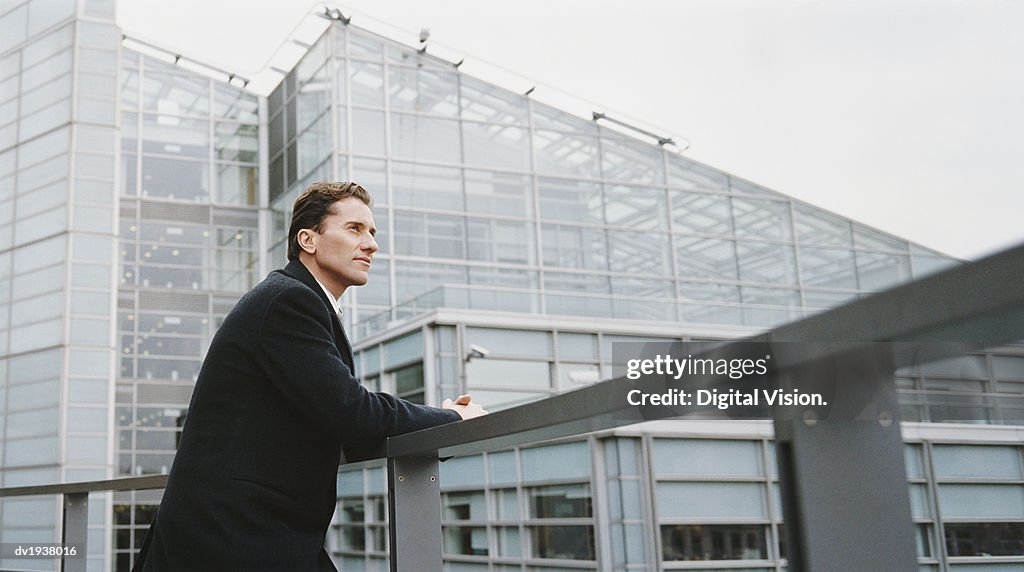Businessman Leaning Against the Railing of a Building and Looking at the View