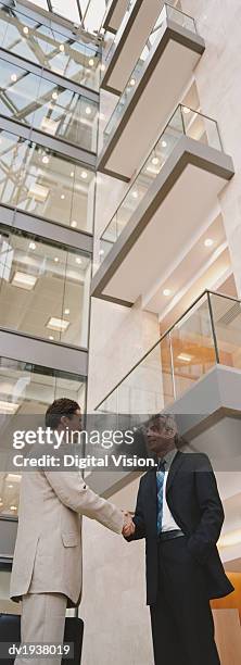 two businessmen shaking hands outside an office building - low angle view of two businessmen standing face to face outdoors stock pictures, royalty-free photos & images