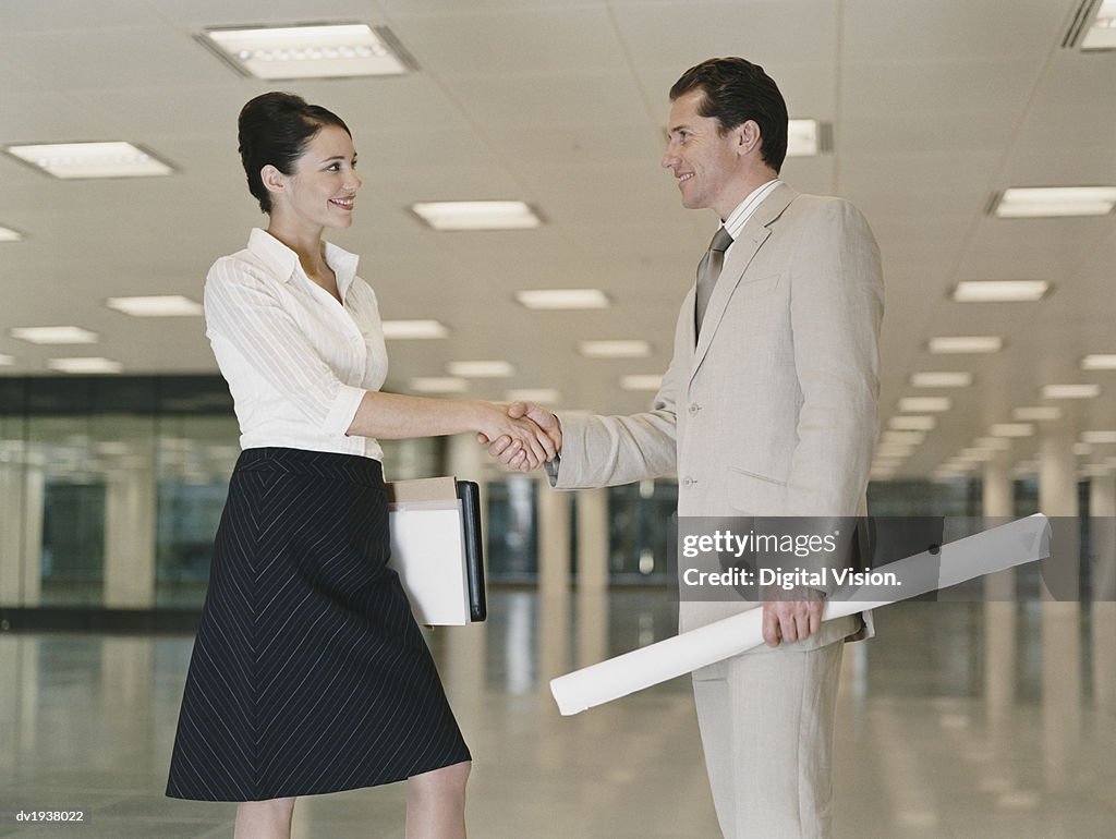 Businessman and Businesswomen Stand in an Empty Office Building Shaking Hands