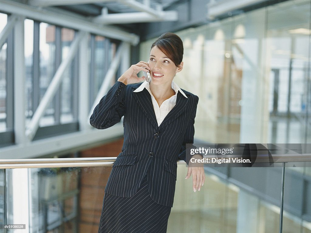 Businesswoman Standing on a Balcony in an Office Building Using a Mobile Phone