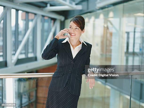 businesswoman standing on a balcony in an office building using a mobile phone - riscas imagens e fotografias de stock