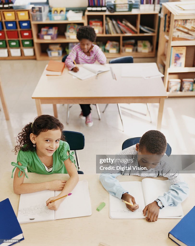 Primary Schoolboys and Schoolgirls Sitting Behind Tables in a Classroom Studying and Writing in Exercise Books