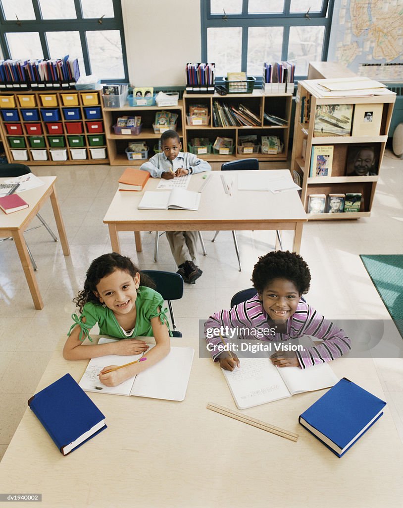 Primary Schoolboys and Schoolgirls Sitting Behind Tables in a Classroom Studying and Writing in Exercise Books