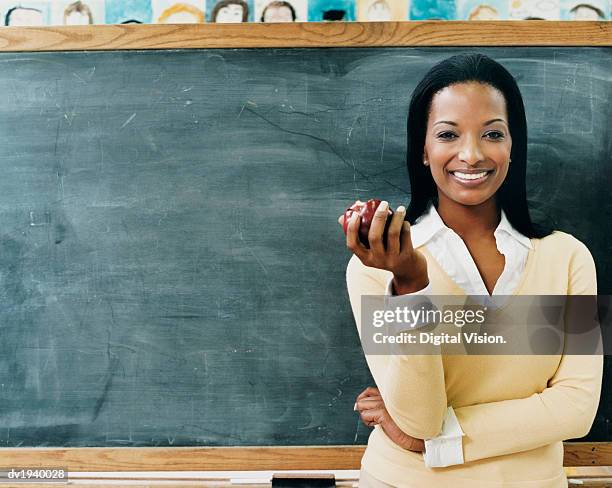 portrait of a teacher standing in front of a blackboard eating an apple - teacher in front of class stock pictures, royalty-free photos & images