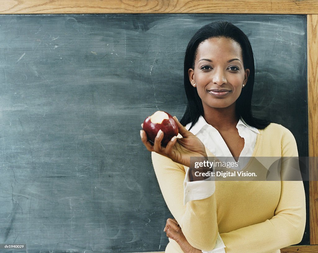 Portrait of a Teacher Standing in Front of a Blackboard Eating an Apple