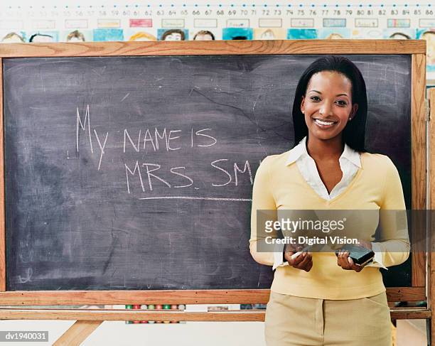 portrait of a teacher standing next to a blackboard in a classroom - long term vision stock pictures, royalty-free photos & images