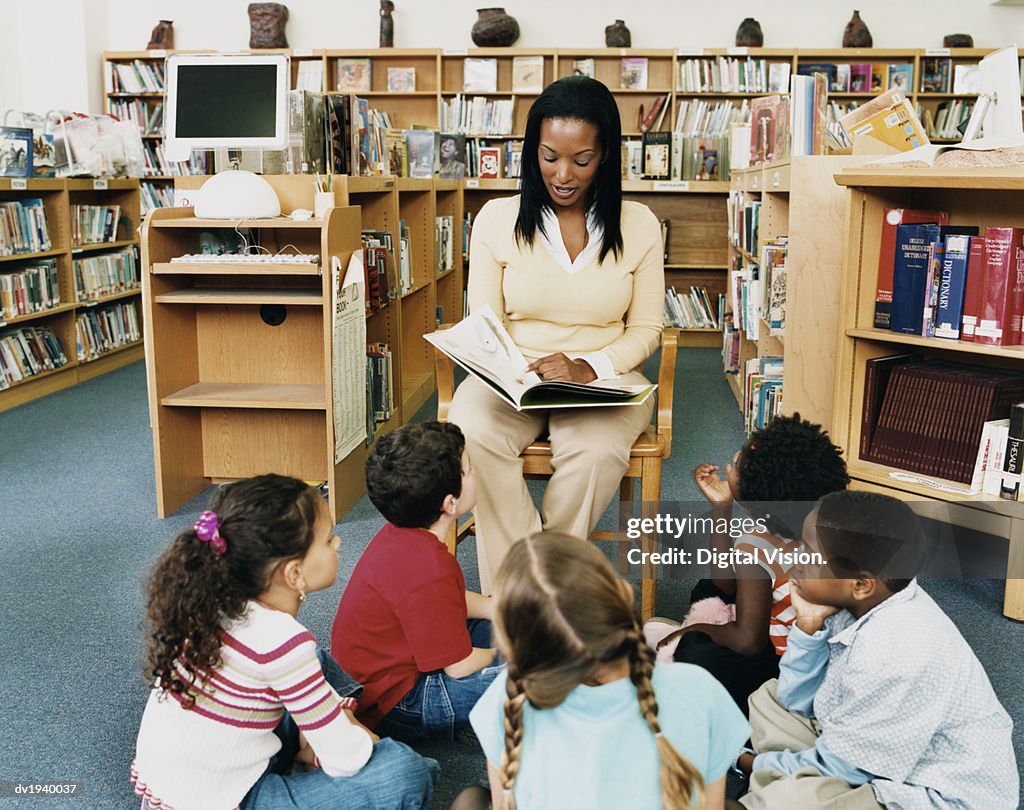 Teacher Reading a Story Book to Children in a Library
