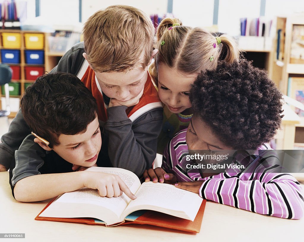 Four Girls and Boys Looking at the Same Textbook in a Classroom at Primary School
