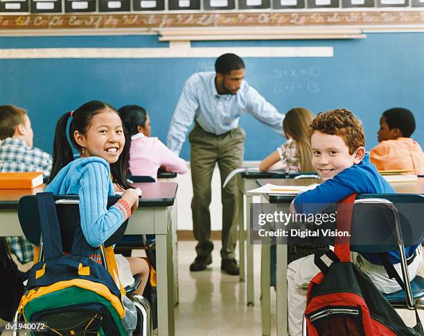 two smiling children sitting at the back of a primary school class - two female teachers blackboard stockfoto's en -beelden