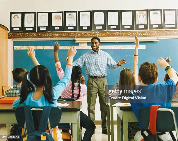 teacher standing in front of a class of raised hands - lagere schoolleeftijd stockfoto's en -beelden