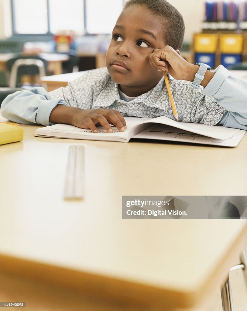 School Boy Sits at a Table With an Exercise Book, Listening and Looking Sideways